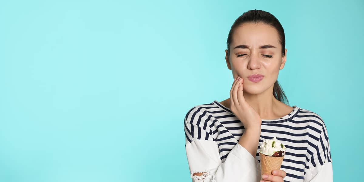 Emotional young woman with sensitive teeth and ice cream on color background. - Forestbrook Dental
